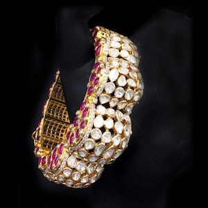 Pode incluir: Um bracelete de ouro com um design de fileiras alternadas de pequenas pedras redondas transparentes e pedras transparentes maiores e facetadas. O bracelete é acentuado com pequenas pedras vermelhas.