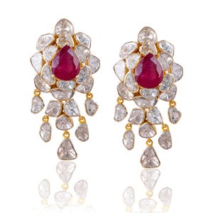 May include: A pair of gold earrings featuring a central pear-shaped deep red gemstone surrounded by multiple irregular, translucent white stones arranged in a floral pattern, with additional dangling white stones suspended from the base.