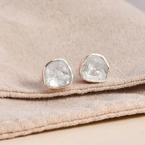 May include: A pair of silver earrings with clear, faceted gemstones set in a hammered metal frame.