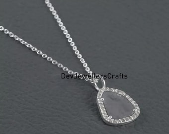 Puede incluir: Un collar de cadena de plata con un colgante que presenta una piedra preciosa gris rodeada por un halo de pequeñas piedras transparentes.