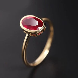Pode incluir: Um anel de ouro com uma grande gema de rubi de forma oval, engastada em uma moldura de bezel.