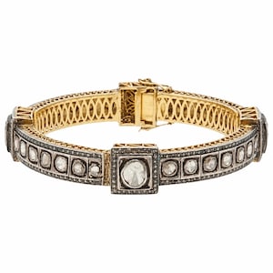 May include: A hinged gold bracelet featuring a series of square settings, each containing a single round-cut stone. The exterior is framed by dark metal borders encrusted with tiny stones, while the interior displays a gold lattice pattern.