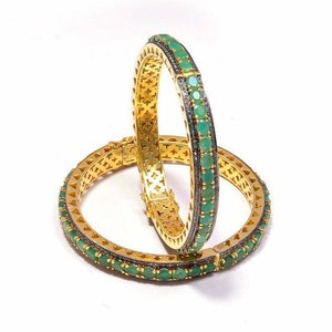 Op de afbeelding: Een paar gouden armbanden met een delicaat ontwerp. Elke armband is versierd met een rij smaragdgroene edelstenen en een rij kleine zilveren kralen.