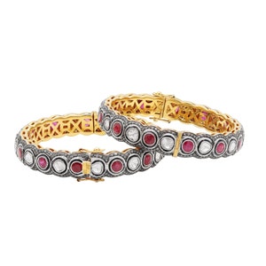 Puede incluir: Un par de brazaletes de oro con un acabado oxidado negro. Los brazaletes están adornados con rubíes rojos redondos y diamantes blancos.