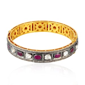 Könnte beinhalten: Goldarmband mit schwarzer Oxidierung. Das Armband ist mit einer Reihe von roten Rubin- und weißen Diamantensteinen verziert.