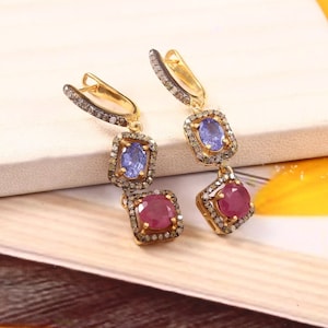 May include: Gold dangle earrings with blue and red gemstones set in a square frame with diamond accents.