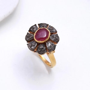 Könnte beinhalten: Ein goldener Ring mit einem roten Rubin-Edelstein, der von einem Blumendesign aus kleineren Diamanten umgeben ist. Die Diamanten sind in Silber gefasst.