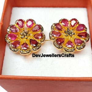 Könnte beinhalten: Ein Paar goldene Ohrringe mit Blumenmuster. Die Ohrringe sind mit rosafarbenen Edelsteinen und kleinen Diamanten besetzt. Die Ohrringe befinden sich in einer kleinen roten Schachtel mit dem Text "DevJewellersCrafts".