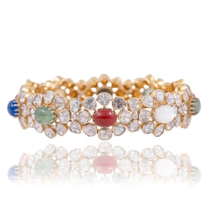 Könnte beinhalten: Ein goldenes Armreif-Armband mit einer Reihe ovaler Edelsteine in verschiedenen Farben, darunter Blau, Grün, Rot und Weiß. Das Armband ist mit kleineren, runden Diamanten besetzt.