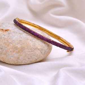 Pode incluir: Um bracelete de ouro com uma fila de pequenas pedras preciosas cor-de-rosa.