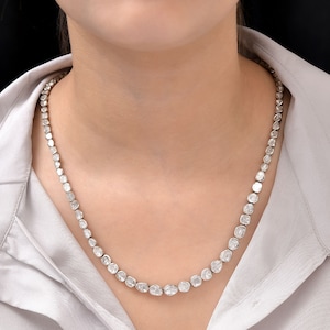 Può includere: Una collana d'argento con una fila di grandi diamanti trasparenti e sfaccettati. I diamanti sono incastonati in una montatura a bezel e sono tutti della stessa dimensione.