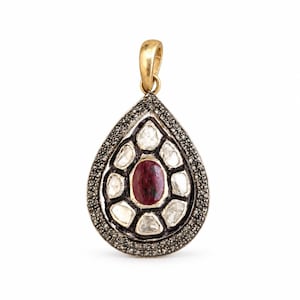 Pode incluir: Um pingente em forma de gota com uma pedra preciosa oval vermelho-escura no centro, rodeada por várias pedras brancas irregulares. A moldura é acentuada com pequenas pedras cinza-escuras e finalizada com um gancho de metal dourado no topo.