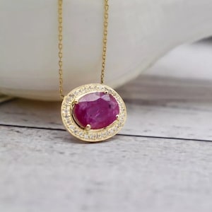 May include: A gold chain necklace with a pendant featuring a large oval ruby surrounded by a halo of smaller diamonds.