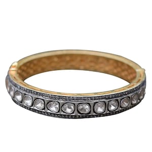 Pode incluir: Um bracelete de prata com uma fila de pequenas pedras redondas e transparentes engastadas em uma banda de metal preto. O bracelete tem um interior dourado.