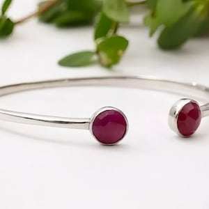 May include: A silver bangle bracelet with two round, deep red gemstones.