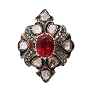 May include: A silver and gold ring with a large red gemstone surrounded by smaller diamonds in a floral design.