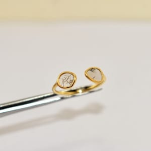 May include: A gold ring with two clear, rough-cut diamonds set in the band. The ring is open and adjustable.