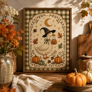 May include: A framed cross-stitch embroidery featuring a white goose wearing a black witch hat and holding a jack-o'-lantern bucket. The design includes a crescent moon, stars, autumn leaves, acorns, and pumpkins, all set against a green gingham border.