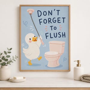 May include: A framed wall art print featuring a white duck with a yellow beak and feet, pulling a chain attached to a ceiling fixture. Next to the duck is a light pink toilet. The text reads, "DON'T FORGET TO FLUSH" in dark blue lettering.