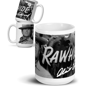 May include: White ceramic mugs featuring black and white images. One mug displays a portrait of a man in a cowboy hat, another shows cattle with the word "RAWHIDE" and a signature, and the third mug has the word "RAWHIDE" and the name "Eastwood".
