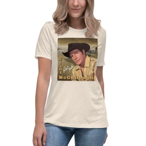 May include: Cream-colored t-shirt featuring a vintage image of actor Flint McCullough in a cowboy hat. The image includes the text "Flint McCullough" and a signature. The shirt is a relaxed fit.