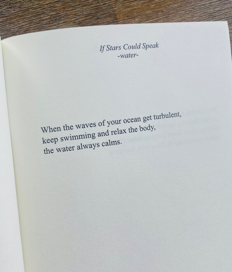 以下が含まれることがあります： 「If Stars Could Speak」と「-water-」のタイトルが書かれた開いた本のページ。困難な時に落ち着きを見つけることについての詩が、読みやすいフォントで印刷されています。