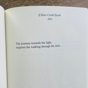 以下が含まれることがあります： 「If Stars Could Speak -fire-」のテキストと引用句「The journey towards the light, requires the walking through the dark.」が書かれた開いた本のページ。クリーム色のページにシンプルなフォントで書かれています。