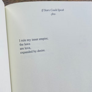 以下が含まれることがあります： 「If Stars Could Speak -fire-」のテキストが書かれた開いた本のページ。詩は「I rule my inner empire; the laws are love, expanded by desire.」と書かれています。テキストはクリーム色のページにシンプルなフォントで書かれています。