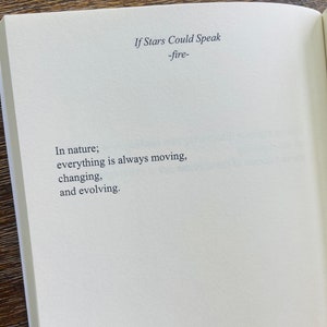 以下が含まれることがあります： 上部に「If Stars Could Speak -fire-」というテキストが表示された開いた本。 「In nature; everything is always moving, changing, and evolving.」というテキストが白いページにセリフ体で印刷されています。