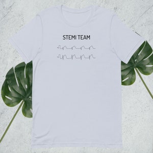 Op de afbeelding: Wit T-shirt met de tekst "STEMI TEAM" en twee EKG-lijnen gedrukt op de voorkant.