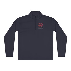 May include: A navy blue long-sleeve performance shirt with a quarter zip closure. The shirt features a red heart with a heartbeat graphic and the text "Cardiac Cath Lab" in white.
