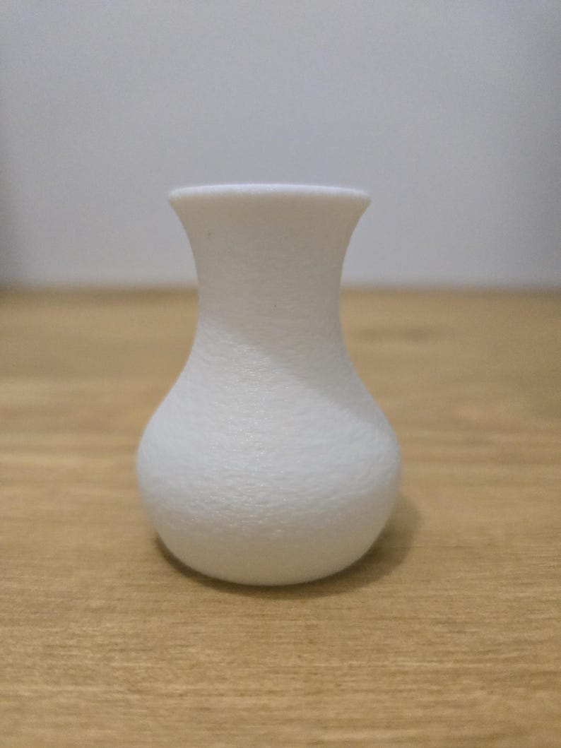 May include: A small, white vase with a textured surface. The vase has a rounded base, a narrow neck, and a flared rim. The vase is approximately 4 inches tall.