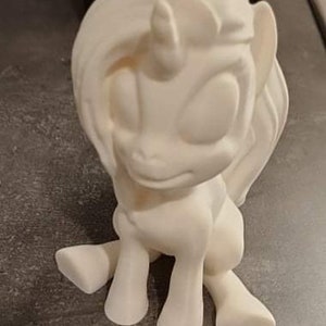 May include: A cream-colored unicorn figurine with a flowing mane and tail, and a single horn. The figurine is in a sitting position, with its front legs extended. The word "HOMEEVER" is visible in the background.