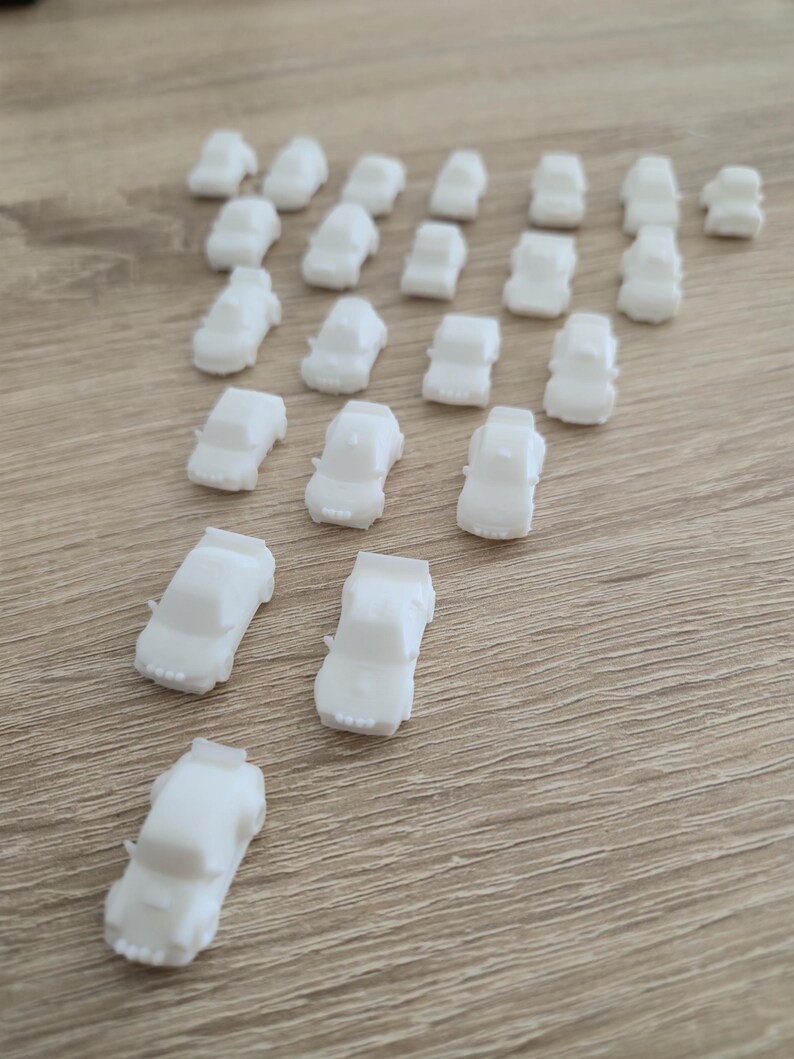 May include: A collection of small, white toy cars arranged on a light brown wooden surface. The cars are uniformly shaped, with a simple design. The arrangement suggests a playful or decorative purpose, possibly for a child's toy set or craft project.