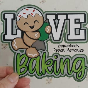May include: Green and white paper craft with the words "LOVE baking" and a gingerbread man holding a green rolling pin. The craft is from Scrapbook Paper Memories.