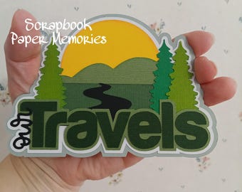 May include: A green and yellow paper craft with the text "Our Travels" and a scene of a sun, mountains, and a river. The text "Scrapbook Paper Memories" is also included.