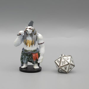 May include: A white miniature figurine of a bear-like creature with a white and brown axe, wearing a green and brown skirt, a red sash, and a gold necklace. The figurine is standing on a black base. A white 20-sided die is in the background.