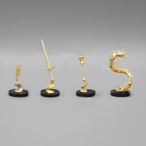 Puede incluir: Cuatro figuritas en miniatura sobre bases negras, cada una representando un objeto de fantasía diferente. Los objetos son una espada, un bastón, una sandalia y una cadena de llamas.