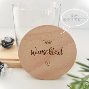 Könnte beinhalten: Ein klares Glas mit einem Holzdeckel. Der Deckel ist rund, hellbraun und trägt den Text "Dein Wunschtext" und ein kleines Herz. Das Bild enthält auch eine Süßigkeitenverpackung und einen Zweig mit Grün.