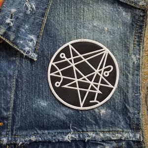 May include: A denim vest with a black and white patch featuring a pentagram symbol. The vest has a Levi's label on the front.