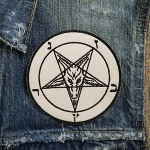 May include: A black and white pentagram patch with a goat's head inside the star. The patch is sewn onto a blue denim vest with frayed edges.