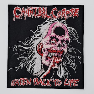 May include: Black square patch featuring the text "CANNIBAL CORPSE" in red above a grotesque, pink-and-white zombie illustration. The text "EATEN BACK TO LIFE" is below the illustration, also in red. The patch is likely for a jacket or bag.