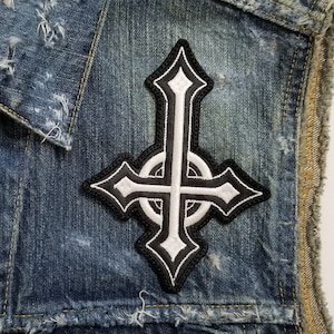 Op de afbeelding: Een blauwe denimvest met een witte en zwarte omgekeerde kruispatch. De vest heeft distressed details en een Levi's label.