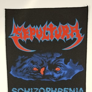 Puede incluir: Parche negro con un logotipo de banda azul y rojo que dice "Sepultura" y una imagen azul y roja de una cara con la palabra "Schizophrenia" debajo. El parche tiene el símbolo de copyright, "1991 Blue Grape Merchandising", y una firma. También dice "Distribuido por Razormatz."