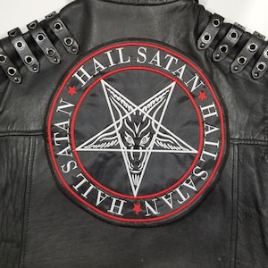 Pode incluir: Colete de couro preto com um grande remendo circular que apresenta um pentagrama com uma cabeça de cabra dentro. O remendo tem o texto "Hail Satan" escrito ao redor do pentagrama em um círculo vermelho com estrelas brancas.