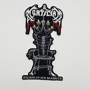 May include: A black embroidered patch featuring the white text MORTICIAN at the top with red blood drips. Below is a chandelier with skulls and candles, a chair constructed from human bones, and the text HACKED UP FOR BARBECUE at the bottom.