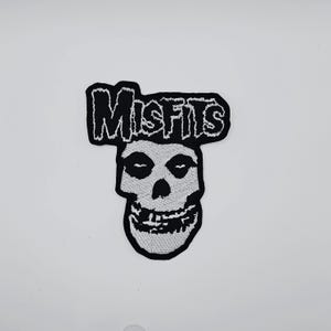 Puede incluir: Parche bordado en blanco y negro con la palabra "Misfits" sobre un gráfico de calavera. El parche tiene un borde negro y está diseñado para coser o planchar sobre ropa o accesorios.
