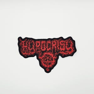 以下が含まれることがあります： ゴシック体で「HORDERIC」と書かれた黒と赤の刺繍パッチ。パッチはユニークな形状と詳細なデザインで、ジャケット、バッグ、その他のアパレルに適しています。