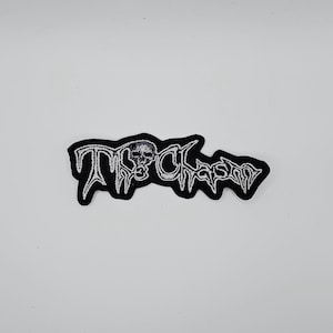 Könnte beinhalten: Schwarz gestickter Aufnäher mit dem Text "TRASHFORM" in einer stilisierten Schriftart, mit einer Totenkopf-Grafik. Der Aufnäher hat einen weißen Rand und ist vor einem weißen Hintergrund platziert.