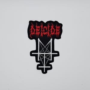 May include: Black and red embroidered patch featuring the word "DEICIDE" in a flame-like font above a white pentagram design. The patch is likely for clothing or accessories.